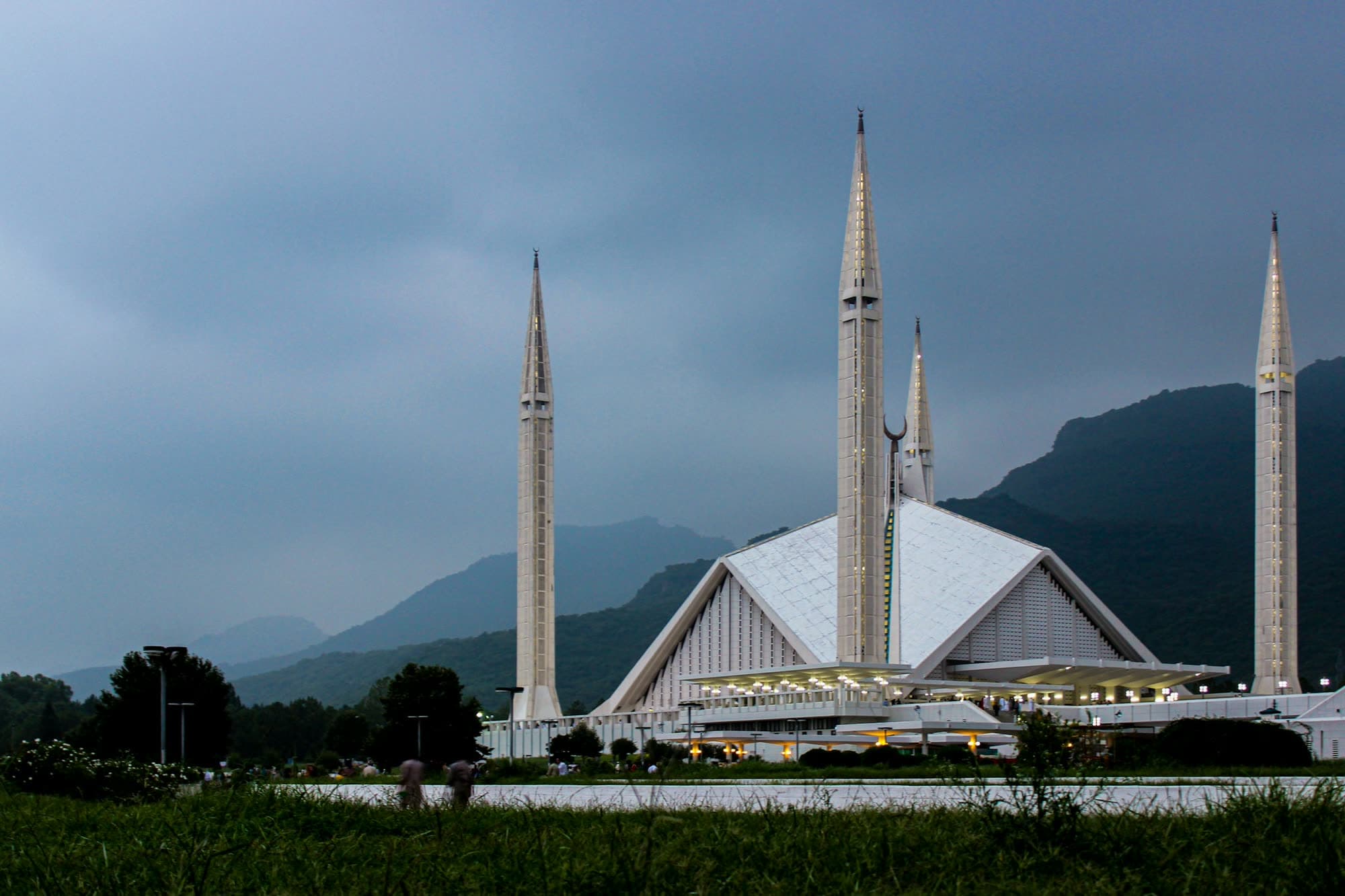 Faisal Mosque in Islamabad, Pakistan, at dusk with tall minarets and mountain backdrop
